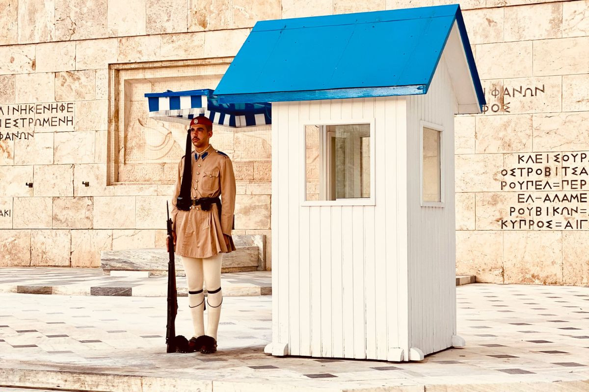 An Evzone guard standing at his post in front of the Tomb of the Unknown Soldier in Athens, wearing a traditional uniform and holding a rifle.